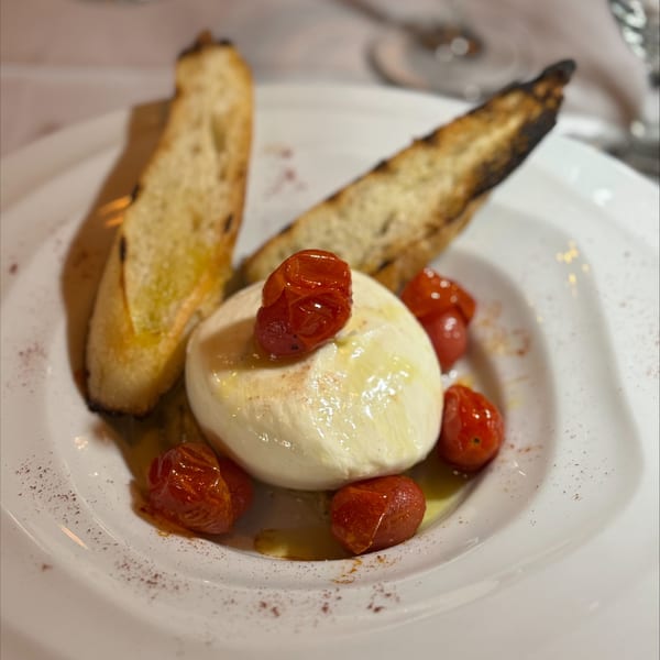 Burrata cheese with roasted cherry tomatoes and toasted bread on a white plate at Janina Bistro.