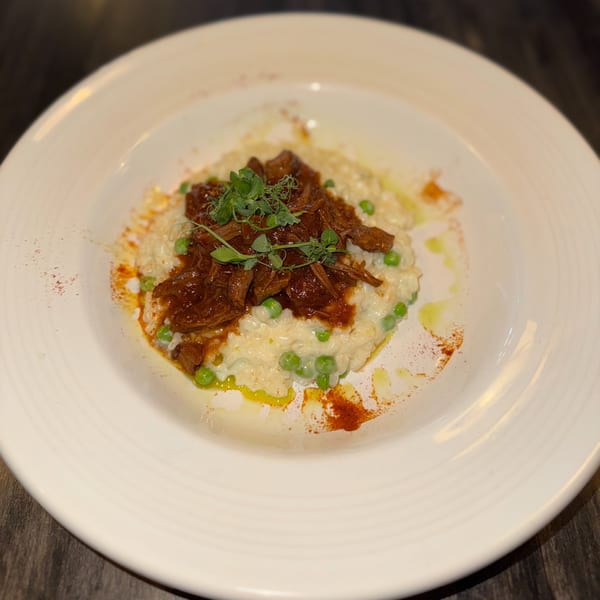 Braised short ribs over creamy risotto with green peas and microgreens, drizzled with oil and paprika.