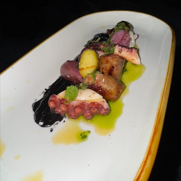 Octopus with potatoes, sausage, and green and black sauces on a white rectangular plate.