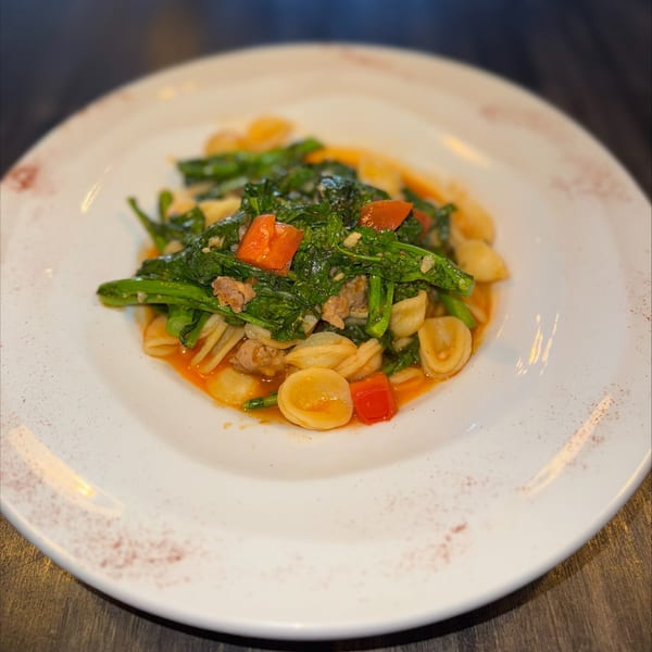Orecchiette pasta with broccoli rabe, tomatoes, and sausage in a light sauce on a white plate.
