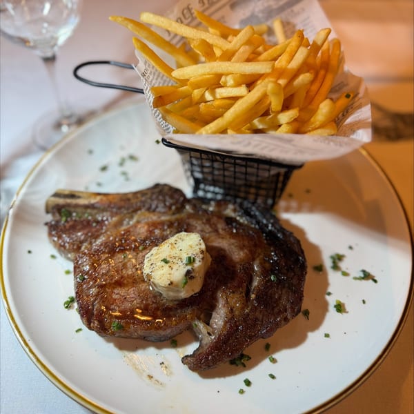 A grilled steak with a pat of butter and a side of french fries in a metal basket.